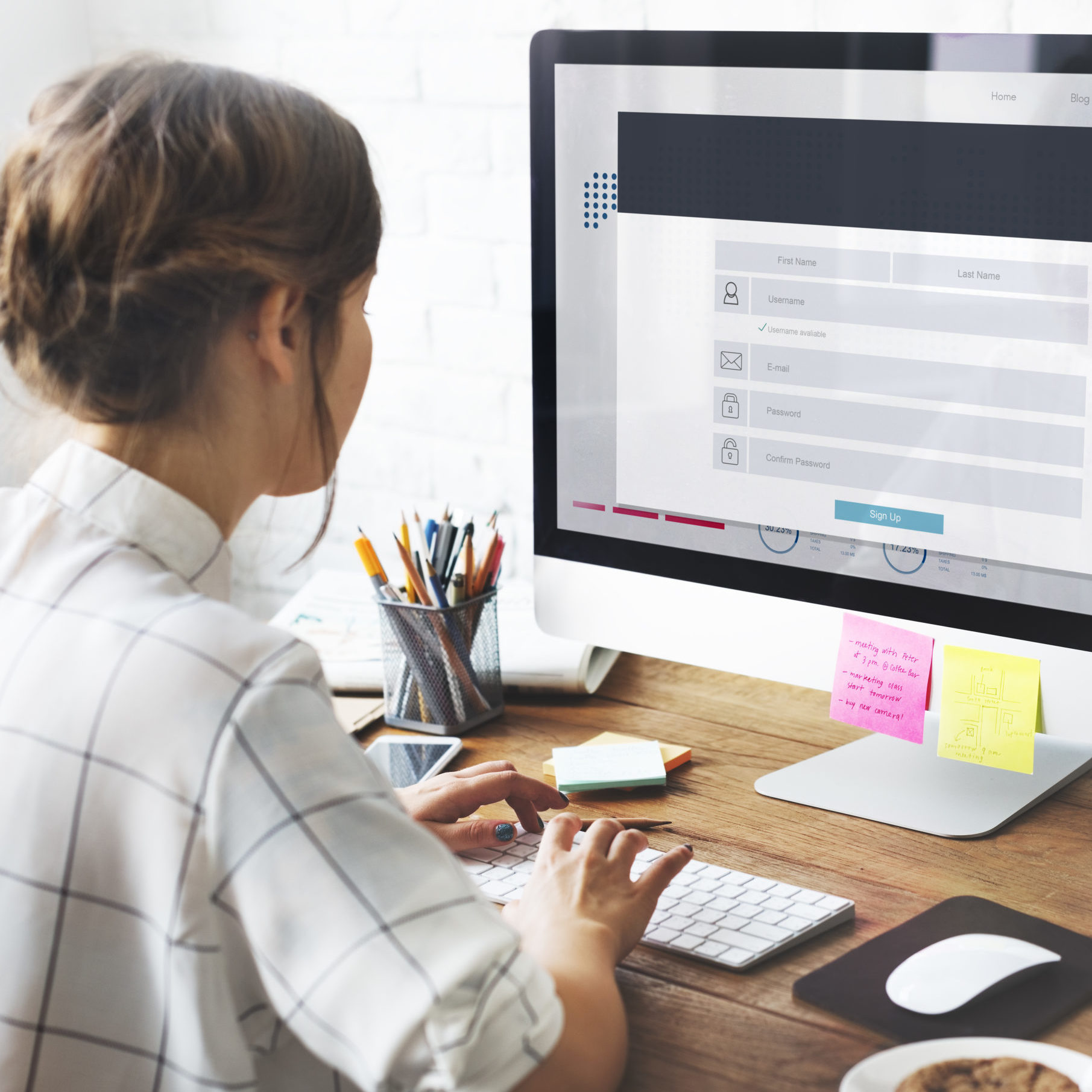 Woman sat at desk filling in a form on a desktop computer with post it notes.